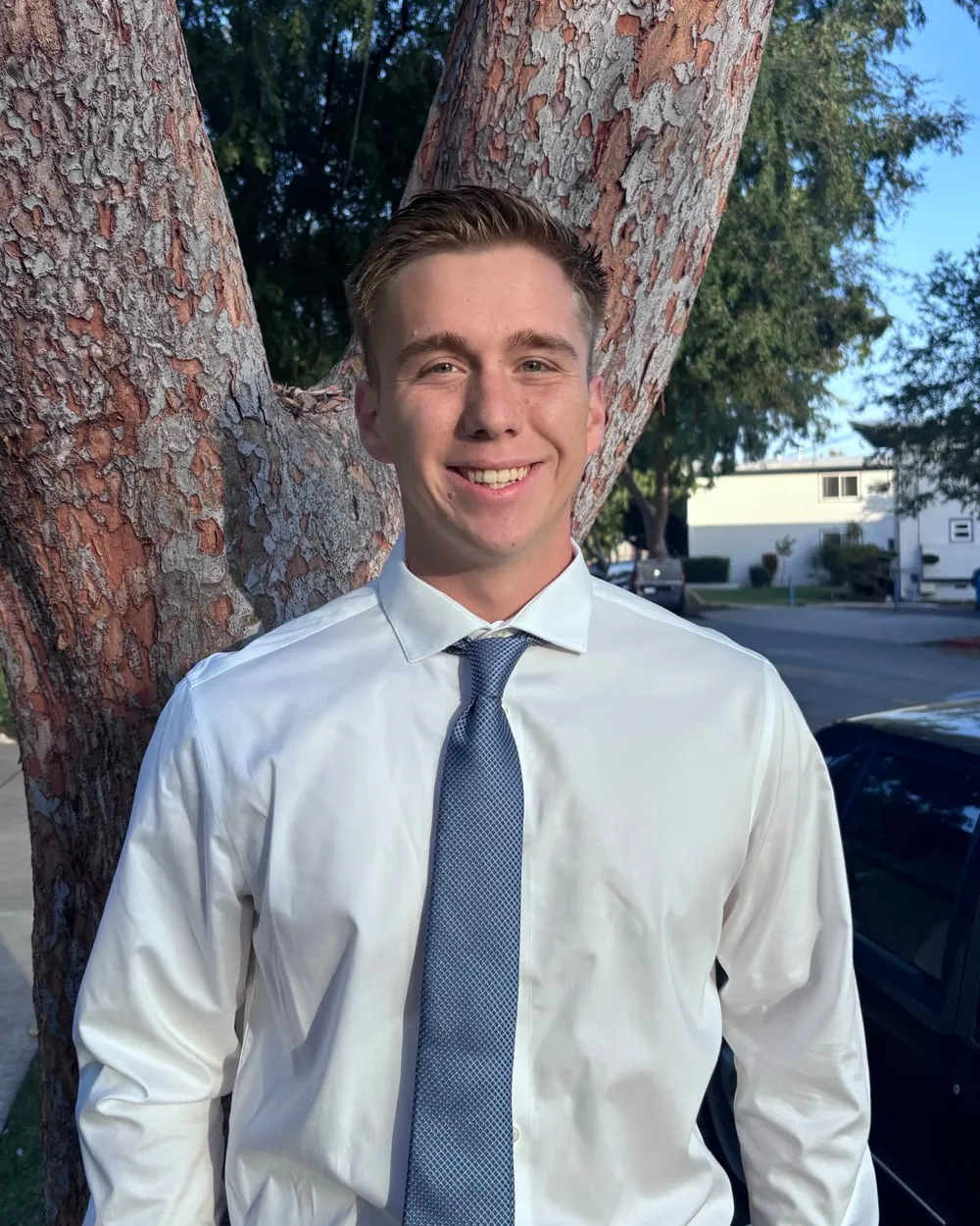Charles Marsh, smiling, in a white shirt and blue tie in front of a tree.